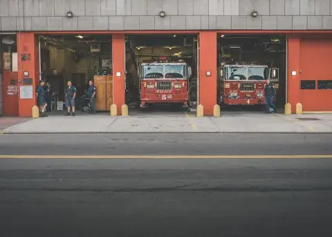 Fire trucks parked in a station with firefighters standing nearby.