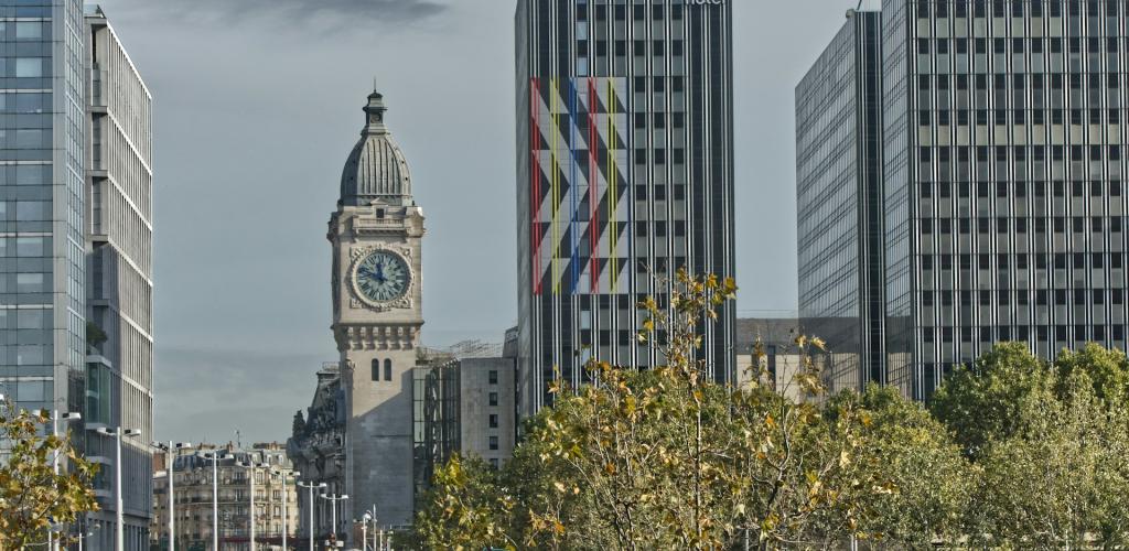 Clock tower beside modern buildings, with trees in foreground.