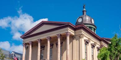 Historic building with columns and clock tower against a blue sky.