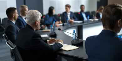 Business meeting with people seated around a conference table with microphones.