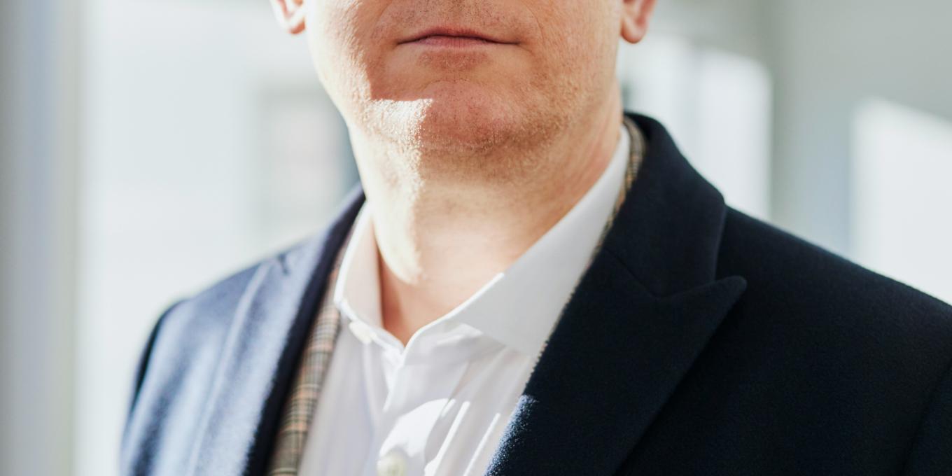 Man in suit and glasses standing in bright office setting.
