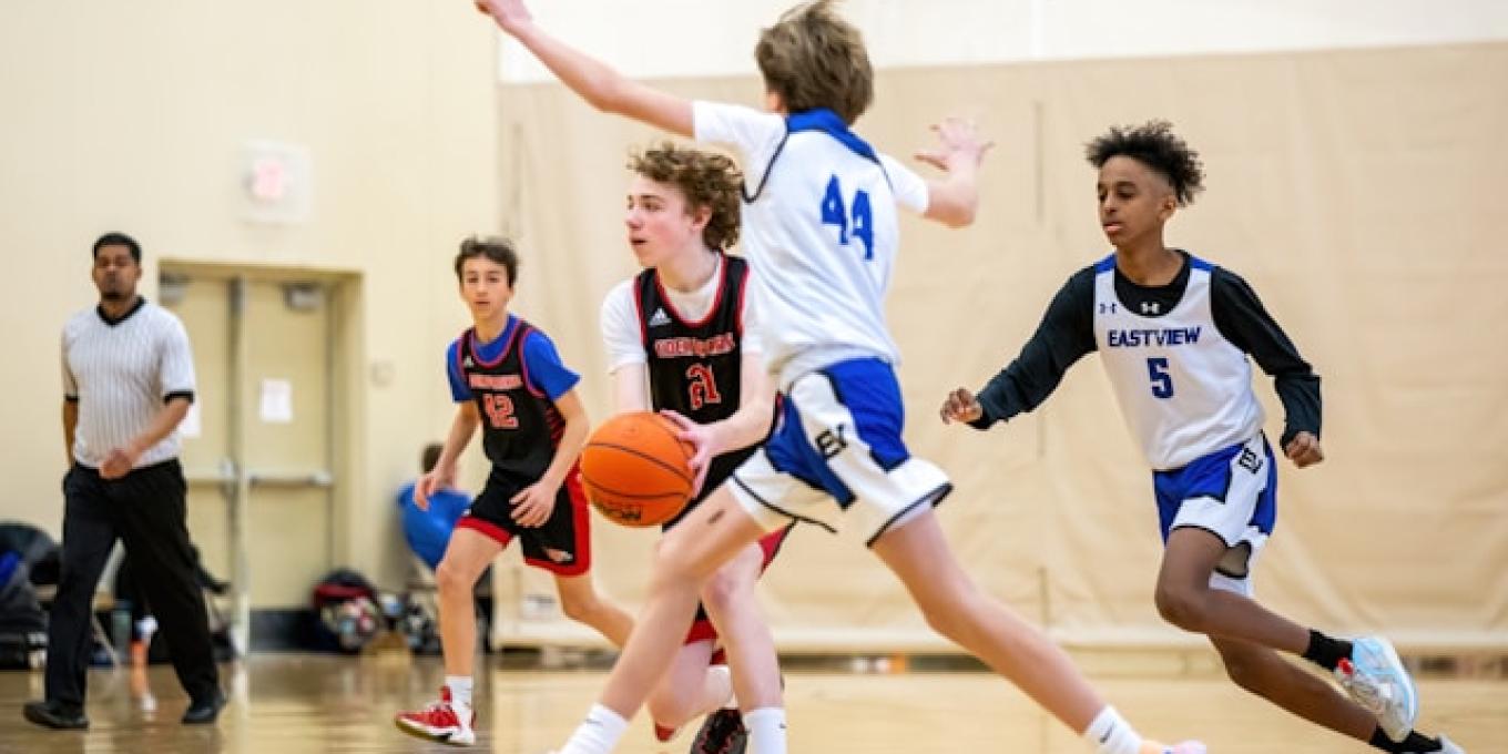 Teen basketball players in action on the court, referee in the background.