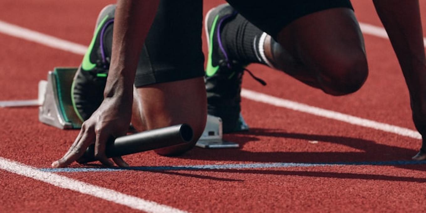 Relay runner at starting blocks on a track, holding a baton.