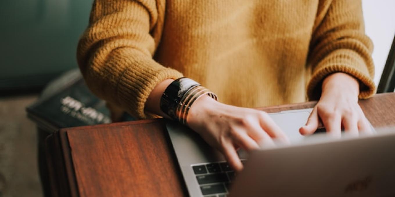 Person typing on a laptop wearing a mustard sweater.