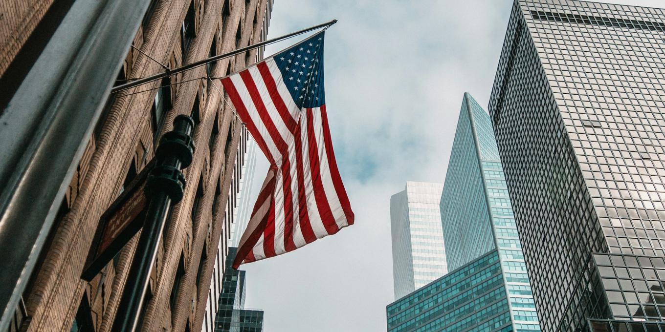 American flag on city building, skyscrapers in background.