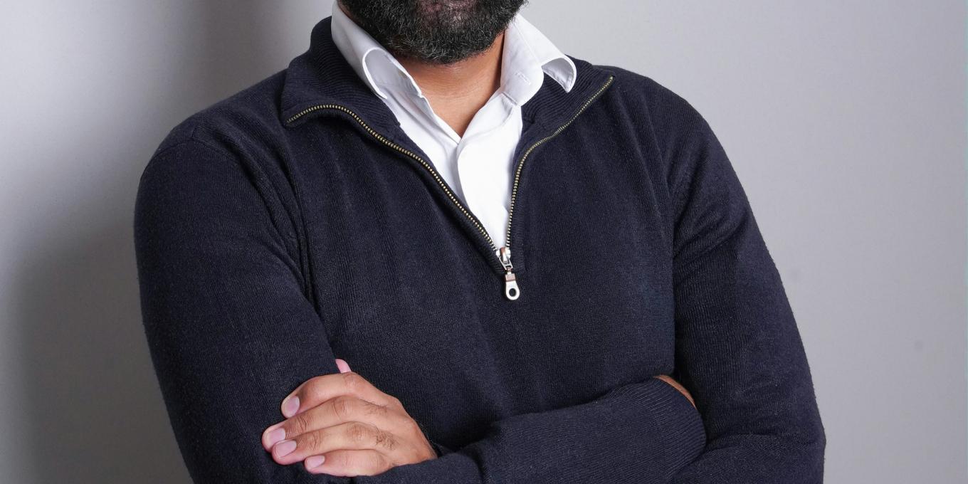 Smiling man with a beard, arms crossed, wearing a black sweater.