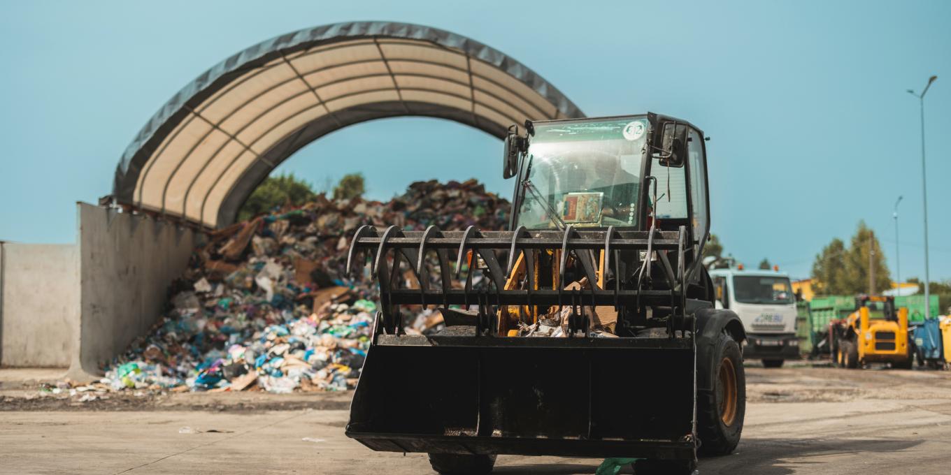 Front loader moving waste near a large pile under a shelter.