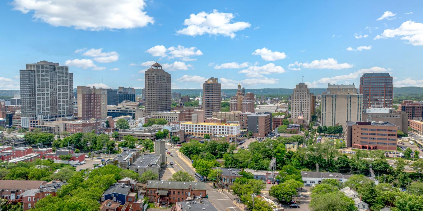 City skyline with tall buildings, blue sky, and scattered clouds.