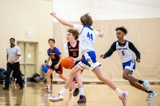 Teen basketball players in action on the court, referee in the background.