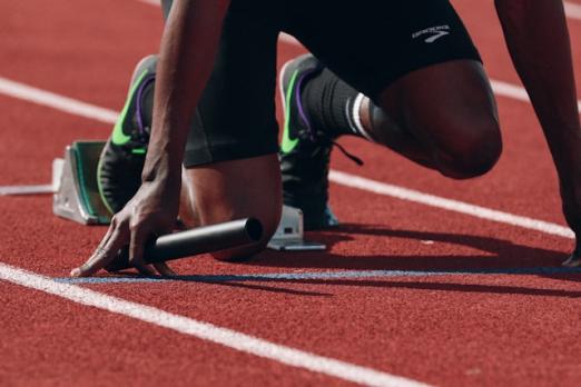 Relay runner at starting blocks on a track, holding a baton.