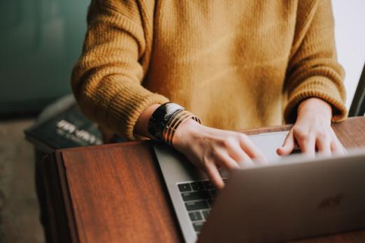 Person typing on a laptop wearing a mustard sweater.