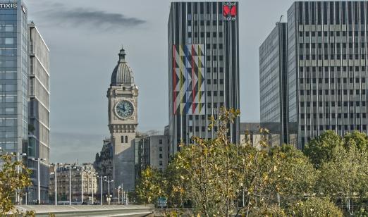 Clock tower beside modern buildings, with trees in foreground.