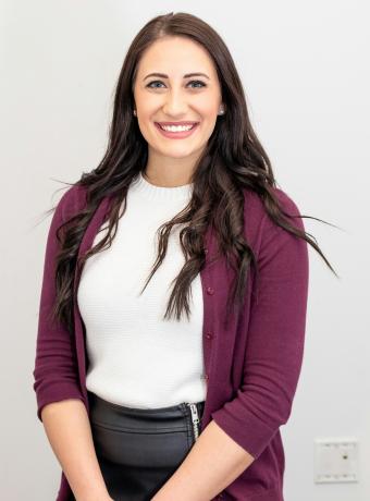 Smiling woman with long dark hair, wearing a maroon cardigan.