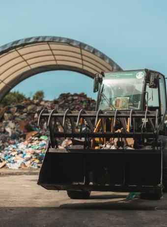 Front loader moving waste near a large pile under a shelter.
