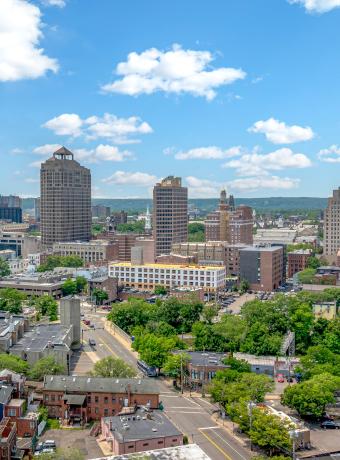 City skyline with tall buildings, blue sky, and scattered clouds.
