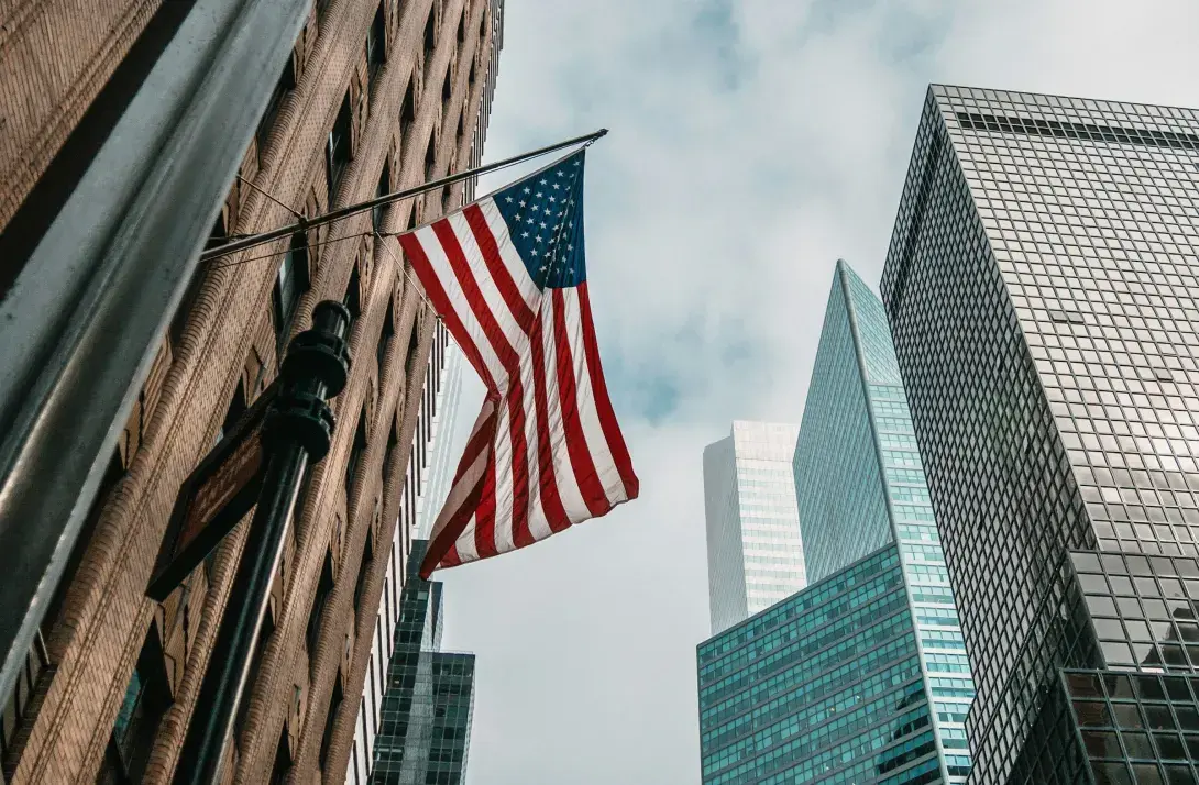 American flag on city building, skyscrapers in background.