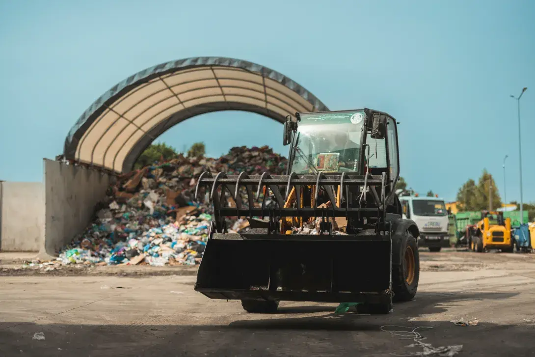 Front loader moving waste near a large pile under a shelter.