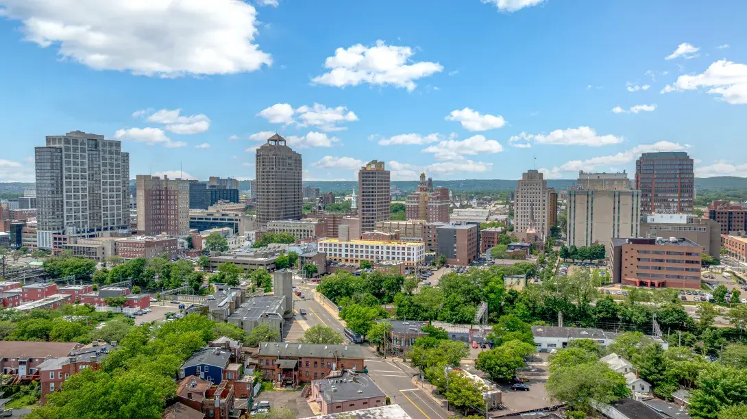 City skyline with tall buildings, blue sky, and scattered clouds.