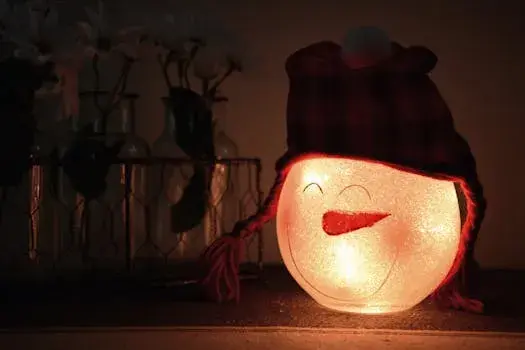 Glowing snowman lamp with a warm hat, surrounded by festive jars indoors, creating a cozy winter atmosphere.
